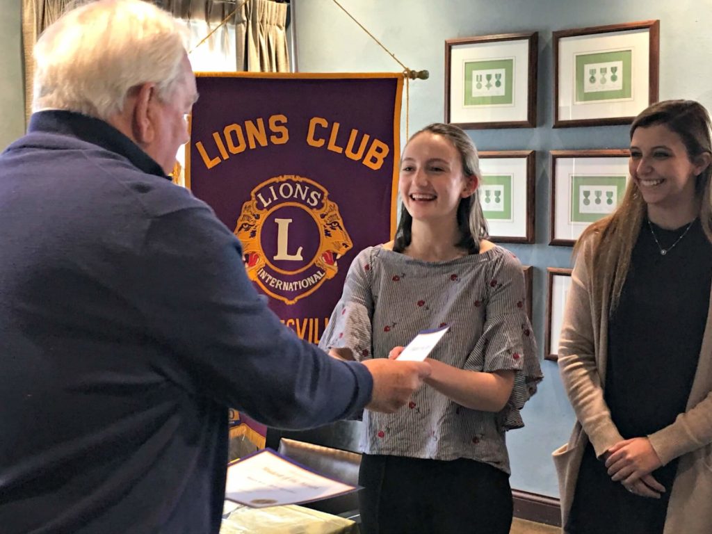 Lion Dennis Steed presents Student of the Month certificates to Sarah Naatz, middle, and Madelyn Byrne.